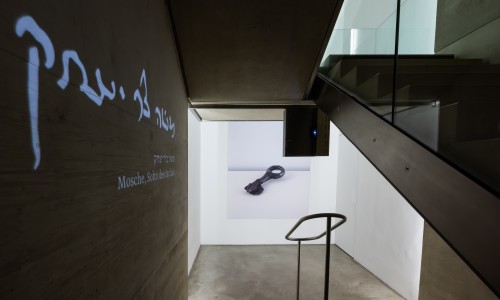 Treppe im Museum mit Projektionsbild einer alten Bronzeschlüssel und hebräischen sowie deutschen Schriftzug 'Mosche, Sohn des Jaakob' an der Wand
