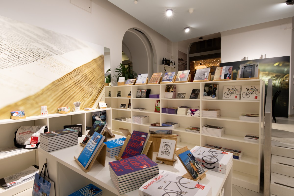 Museumsshop im Jüdischen Museum Wien: Innenraum des Museumsshops mit weißen Regalen und Tischen, auf denen Bücher, Kataloge und Postkarten ausliegen