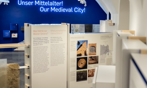 Ausstellungsraum mit Informationstafeln zum mittelalterlichen Wien und leuchtender Aufschrift 'Unser Mittelalter! Our Medieval City!' an blauer Wand