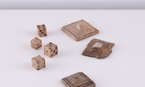 Vier alte Würfel mit erhabenen Punkten und drei abgenutzte quadratische Spielsteine auf weißem Untergrund