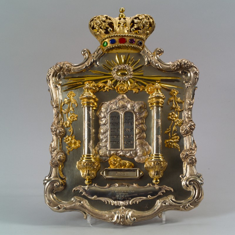 Silvernes dekoratives Schild mit goldenen Verzierungen, zwei Säulen, einer Krone oben mit bunten Steinen, einem Löwen und den Zehn Geboten in hebräischer Schrift
