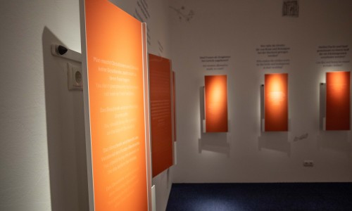 Orangefarbene Informationstafeln mit Text an weißen Wänden in einem Raum des Jüdischen Museums Wien