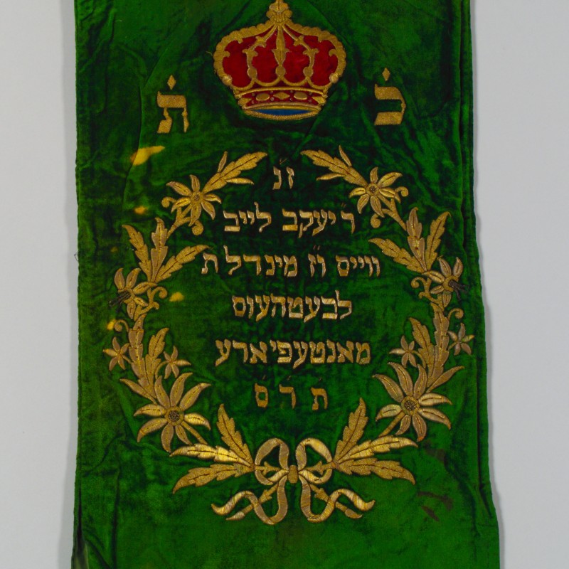 Grünes Stoffbanner mit goldener Krone oben und goldener floralem Lorbeerkranz mit hebräischer Schrift in der Mitte
