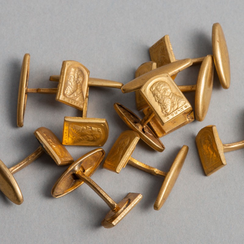 Acht goldene Manschettenknöpfe mit eingravierten Portraits von Männern mit Bart auf rechteckigen Platten