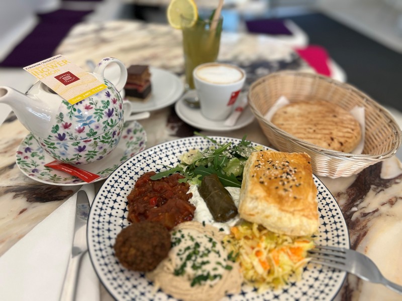 Mediterranean dish with puff pastry and hummus: Mediterranean meal on a patterned plate featuring puff pastry, stuffed grape leaf, hummus, salad, ratatouille, with flatbread in a basket beside it