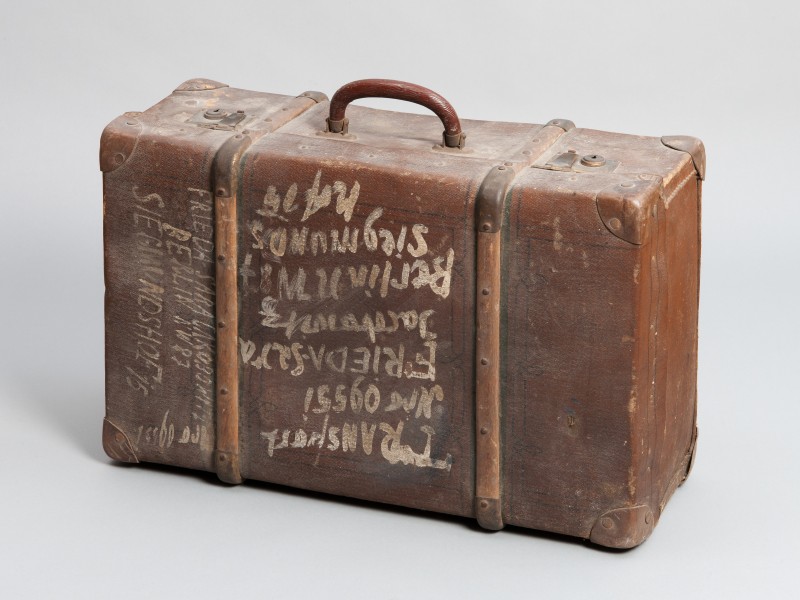 Alte, abgenutzte braune Reisetasche mit handschriftlichen weißen Schriftzügen auf der Vorderseite und seitlich.