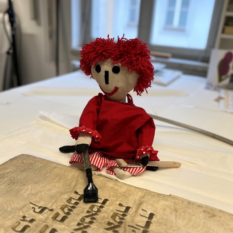 Rote Puppe neben hebräischem Manuskript: Rote Puppe mit roten Wollhaaren und rotem Kleid neben einem alten Manuskript mit hebräischer Schrift
