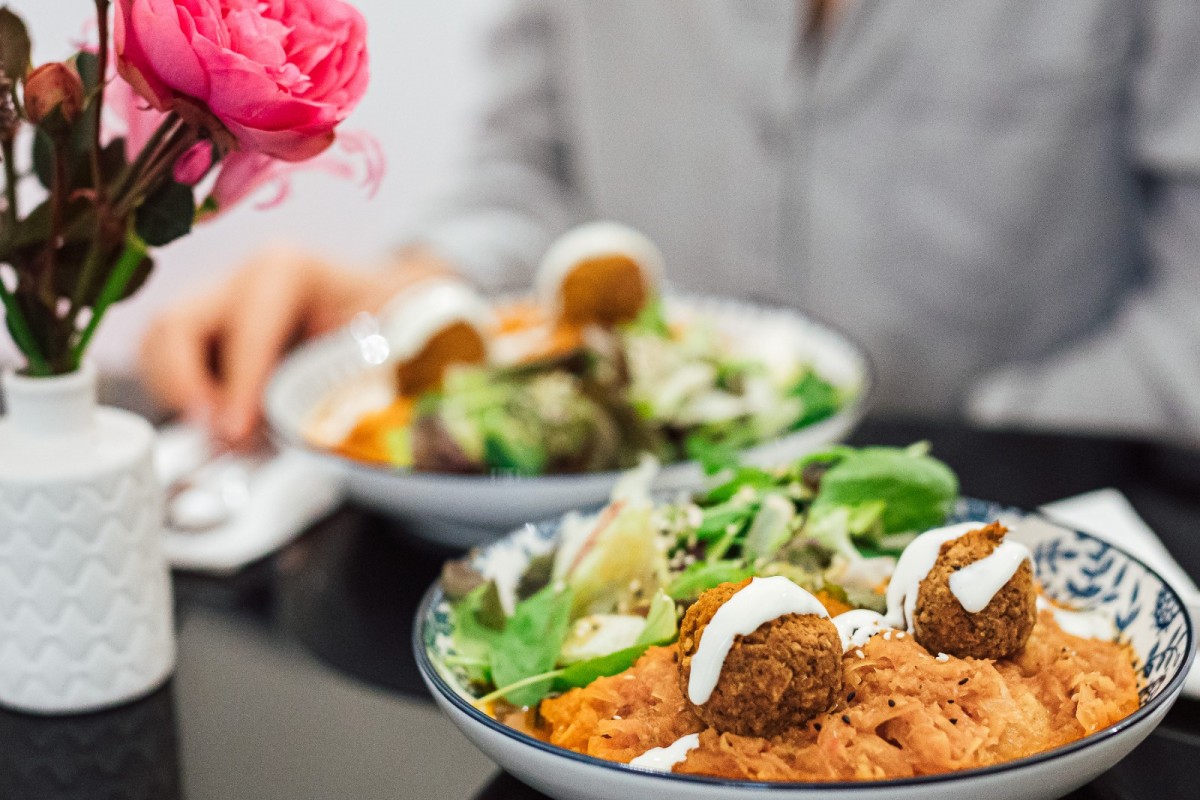 Falafel bowl with salad and sweet potato mash: Close-up of two bowls with falafel, sweet potato mash, and salad on a black table, pink rose in a white vase to the left