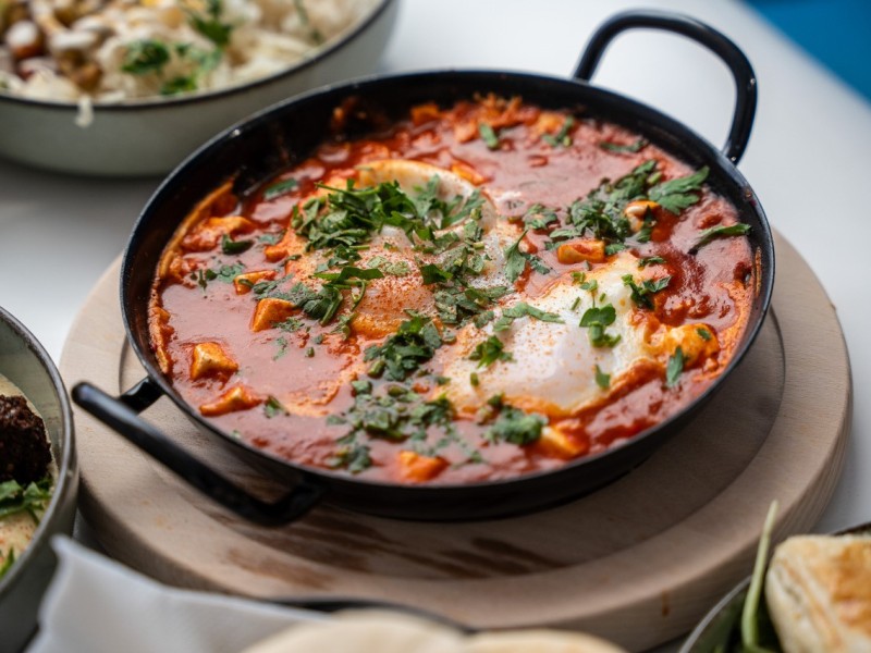 Shakshuka in Pfanne: Schwarze Pfanne mit Shakshuka, Tomatensoße, pochierten Eiern und gehacktem Koriander