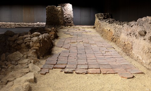 Antike Pflasterung mit quadratischen Ziegelsteinen und niedrigen Steinmauern in einer Innenraum-Archäologie-Ausstellung