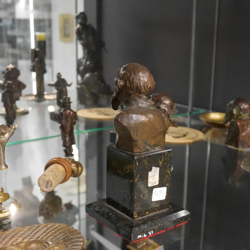 Vitrinenausstellung mit kleinen Bronze- und Metallfiguren, darunter mehrere menschliche Büsten, Figuren mit erhobenen Armen und eine Kerzenhalterfigur