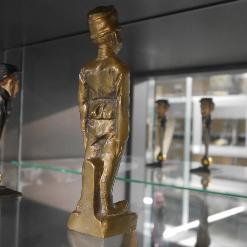 Sechs kleine Statuetten auf einem Glasregal, davon drei in schwarzer und drei in goldener Farbe, in Reihen angeordnet.