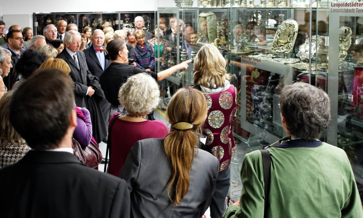 Führung im Leopoldstädter Tempel Museum: Gruppe von Erwachsenen folgt Führung im Museum vor Vitrinen mit Silber- und Metallobjekten, Schild "Leopoldstädter Tempel" sichtbar