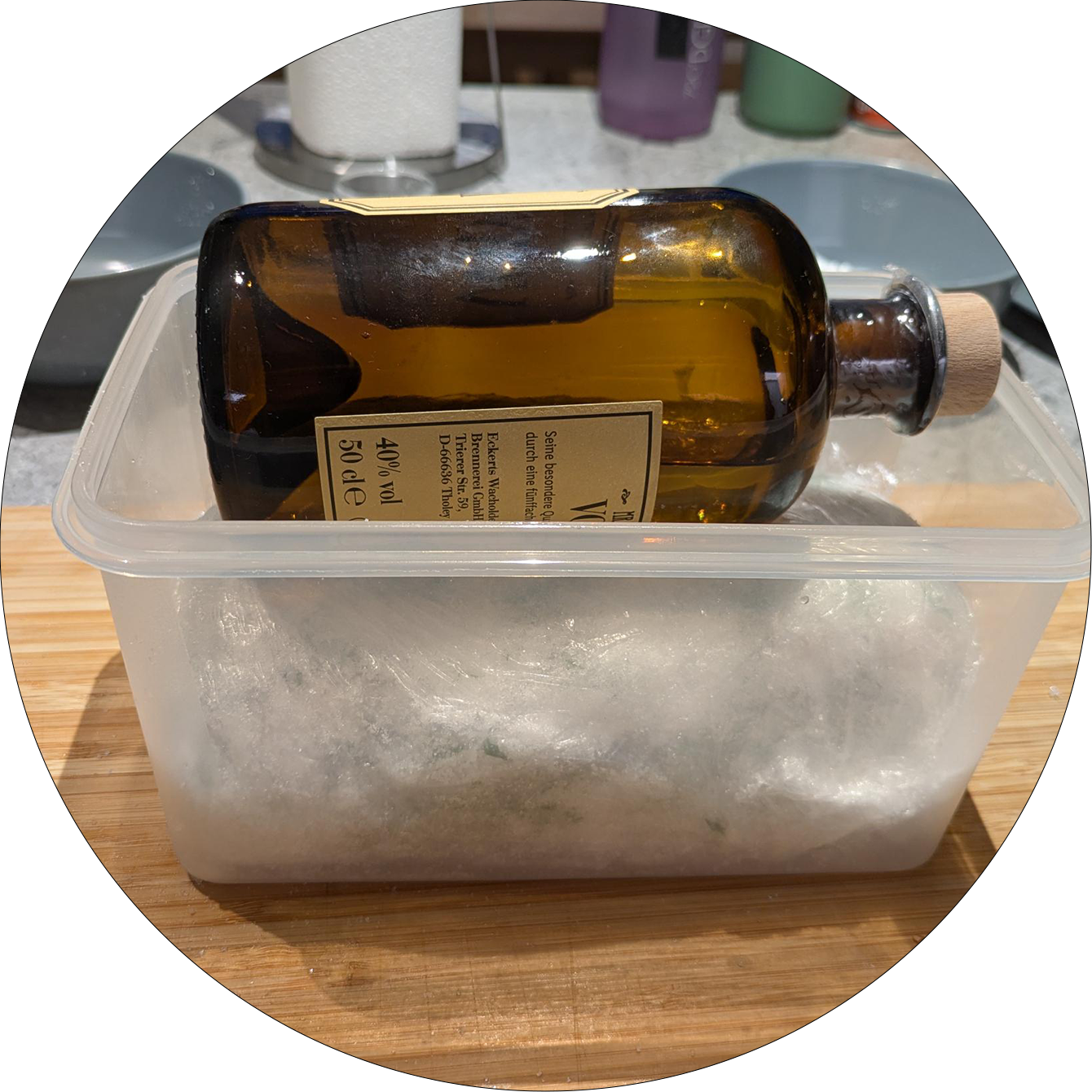 Brown glass bottle with cork stopper lying on a salmon portion wrapped in plastic wrap inside a clear plastic container on a wooden board